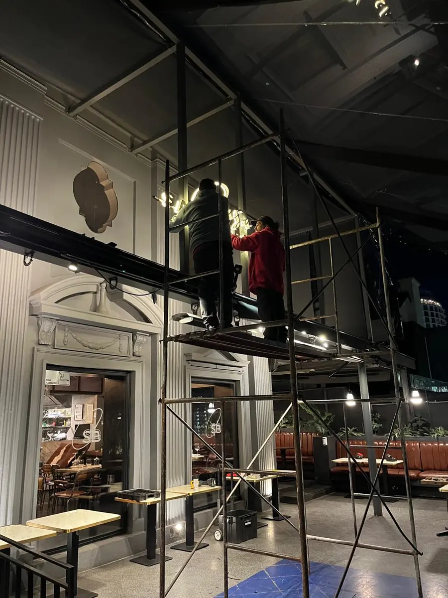 Equipo instalando letras luminosas sobre andamio en la fachada de un restaurante